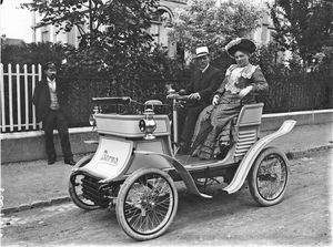 Die Fotografie zeigt einen Mann und eine Frau, welche im vom Kunstschlosser Joseph Wyss konstruierten Automobil, posieren.