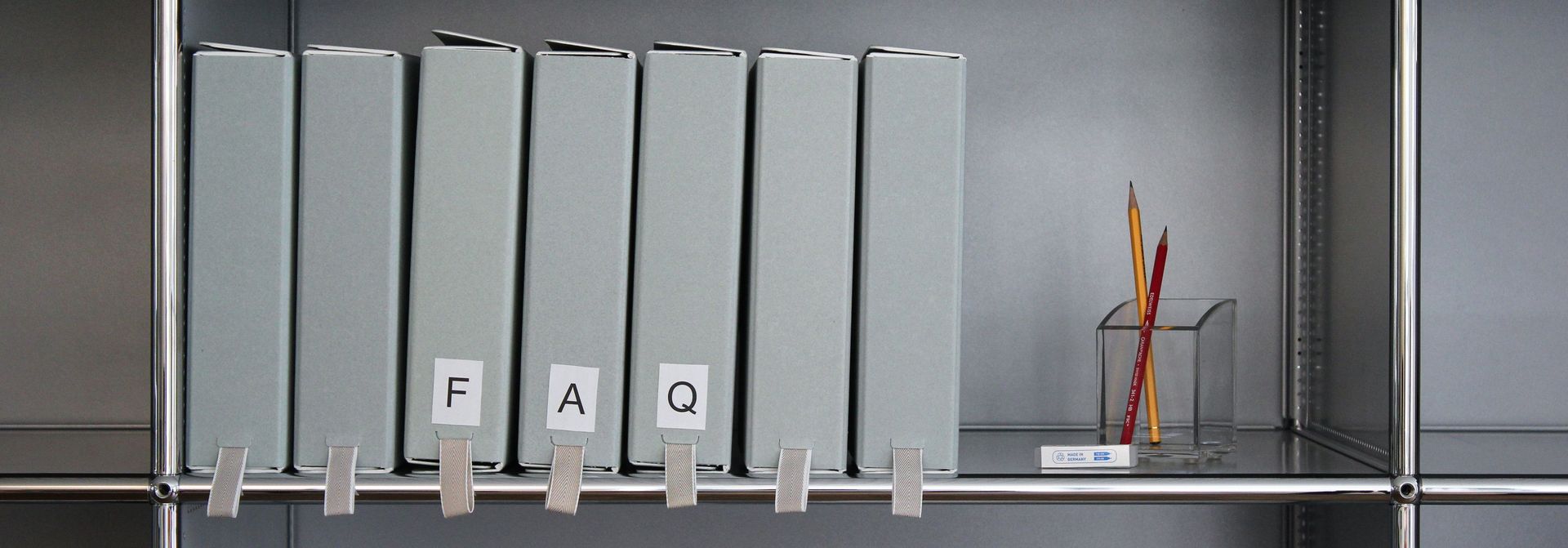 Archivschachteln, welche in einem Regal stehen. Die Schachteln sind mit den Buchstaben F A Q beschriftet.