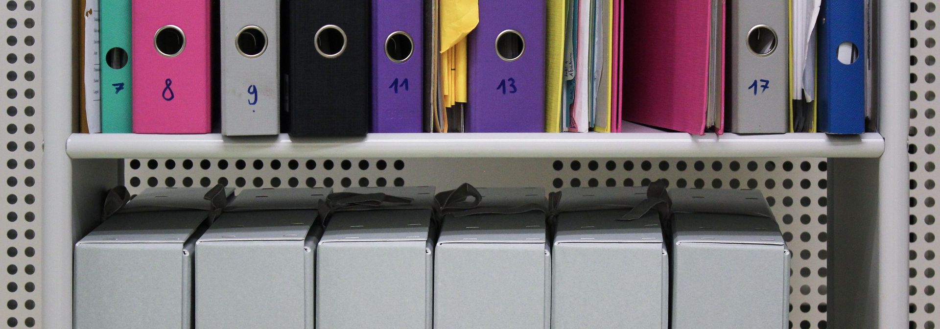 Archivschachteln und Ordner in einem Gestell.