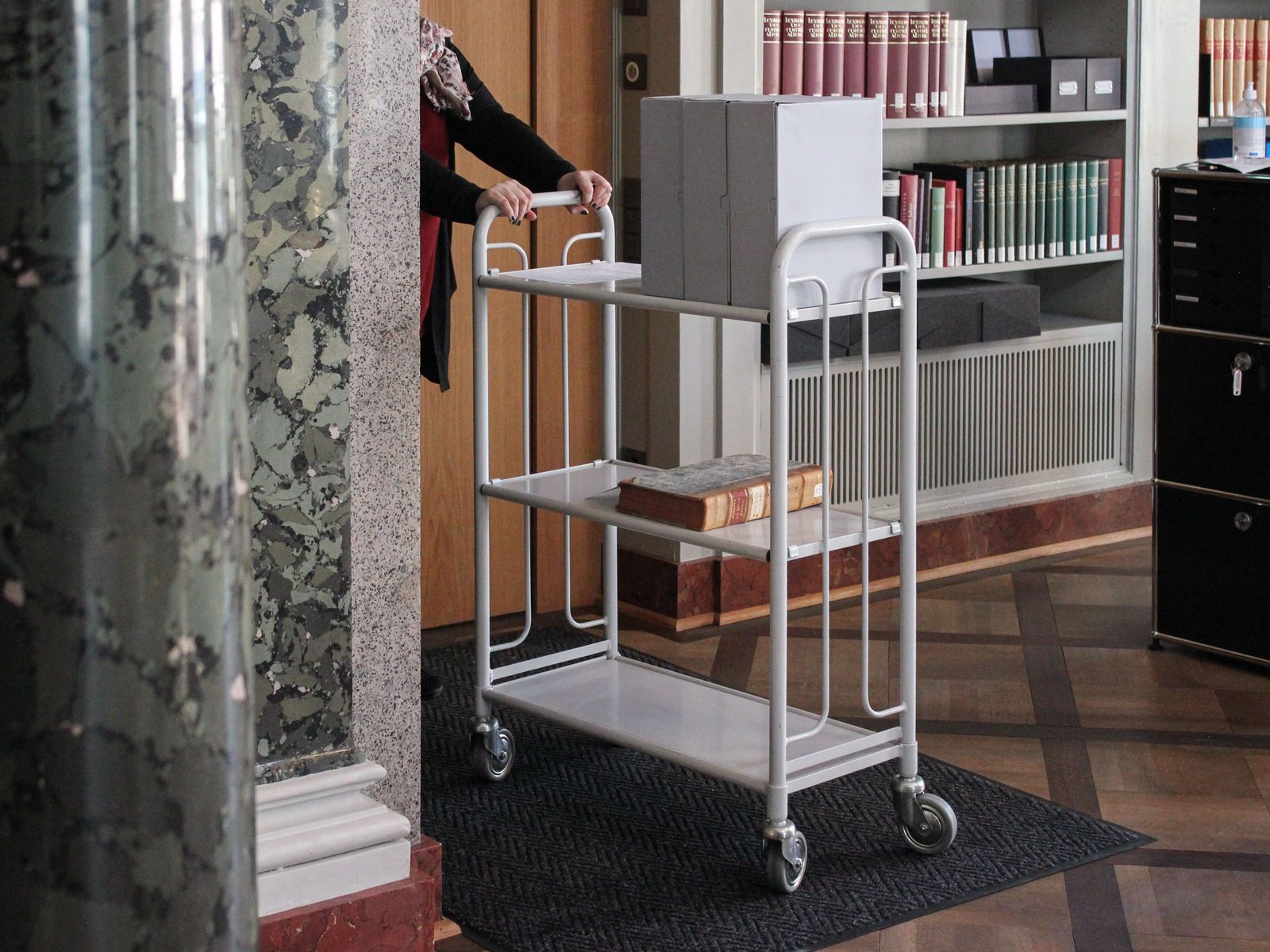Eine Mitarbeitende der Burgerbibliothek bringt die bestellten Akten aus dem Magazin.