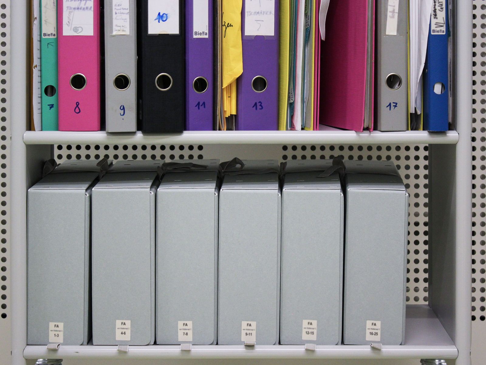 Metallregal: Auf dem höheren Tablar stehen Ordner, auf dem unteren Archivschachteln.